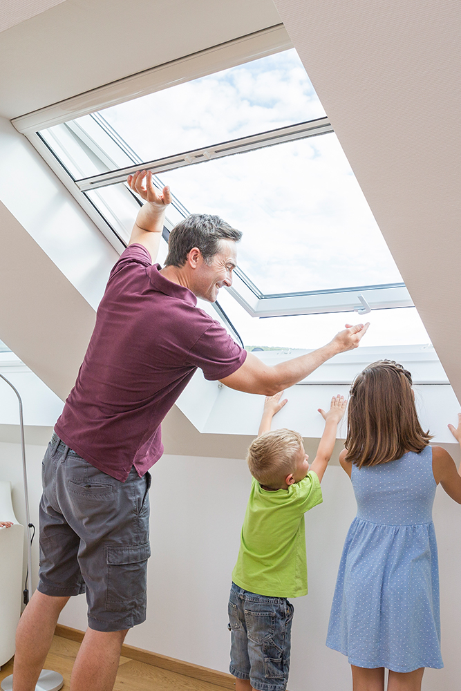Mann mit zwe Kindern, dier gerade ein Fliegengitter für Dachfenster öffnen